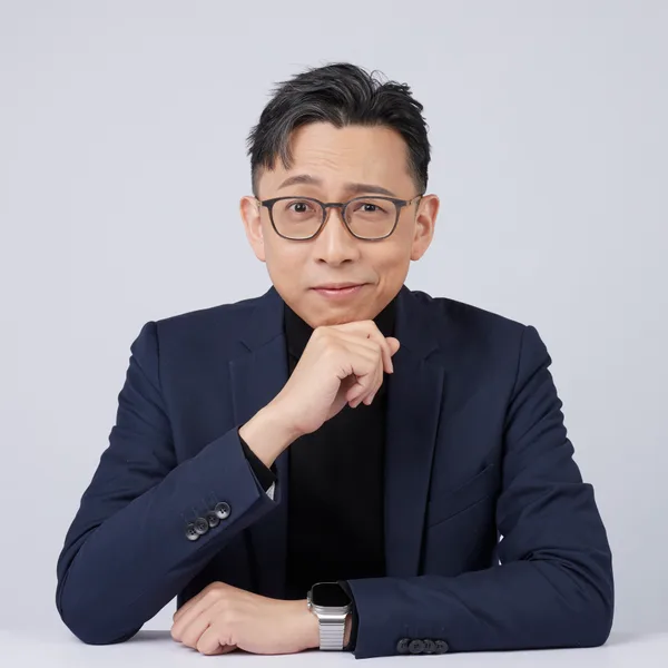 Ju-Chun Ko in a navy suit: chin-on-hand portrait