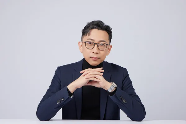 Ju-Chun Ko in a navy suit: hands-folded portrait